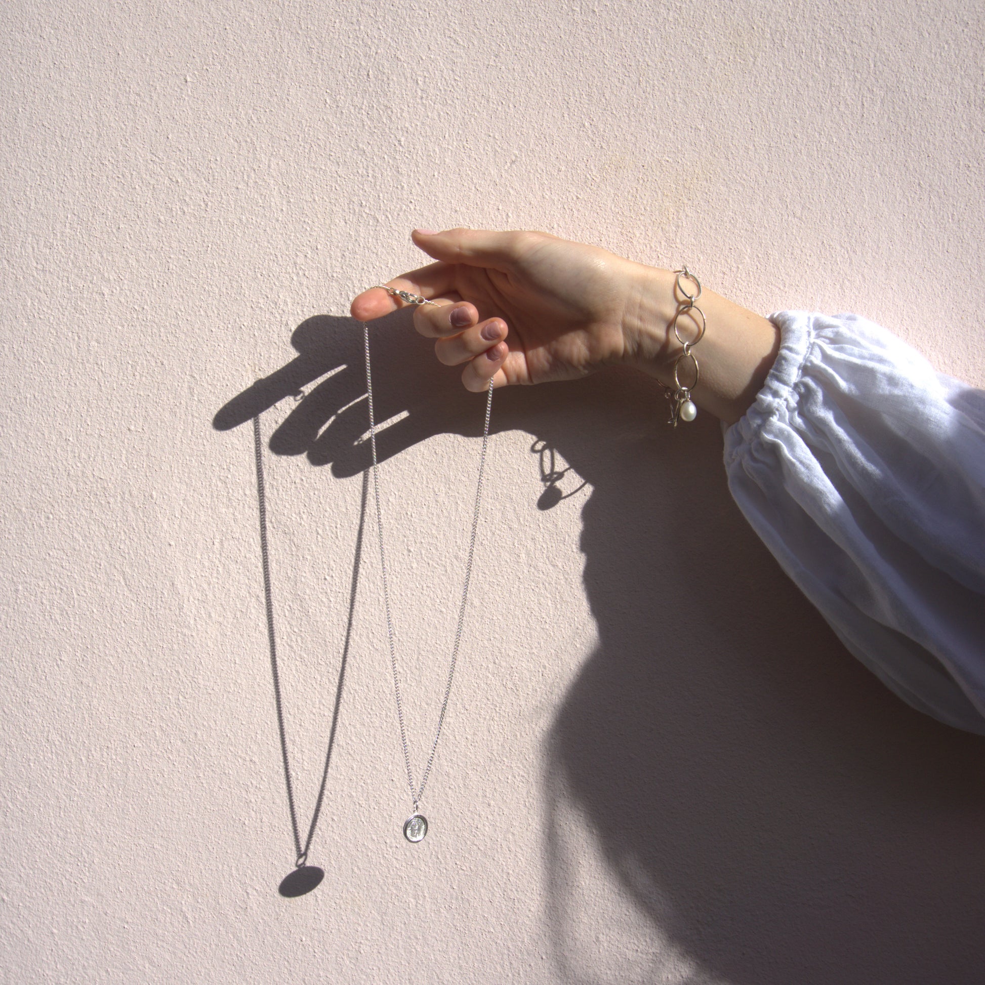 Madeleine holding the St. Christopher necklace against a  pink background in Oxford.