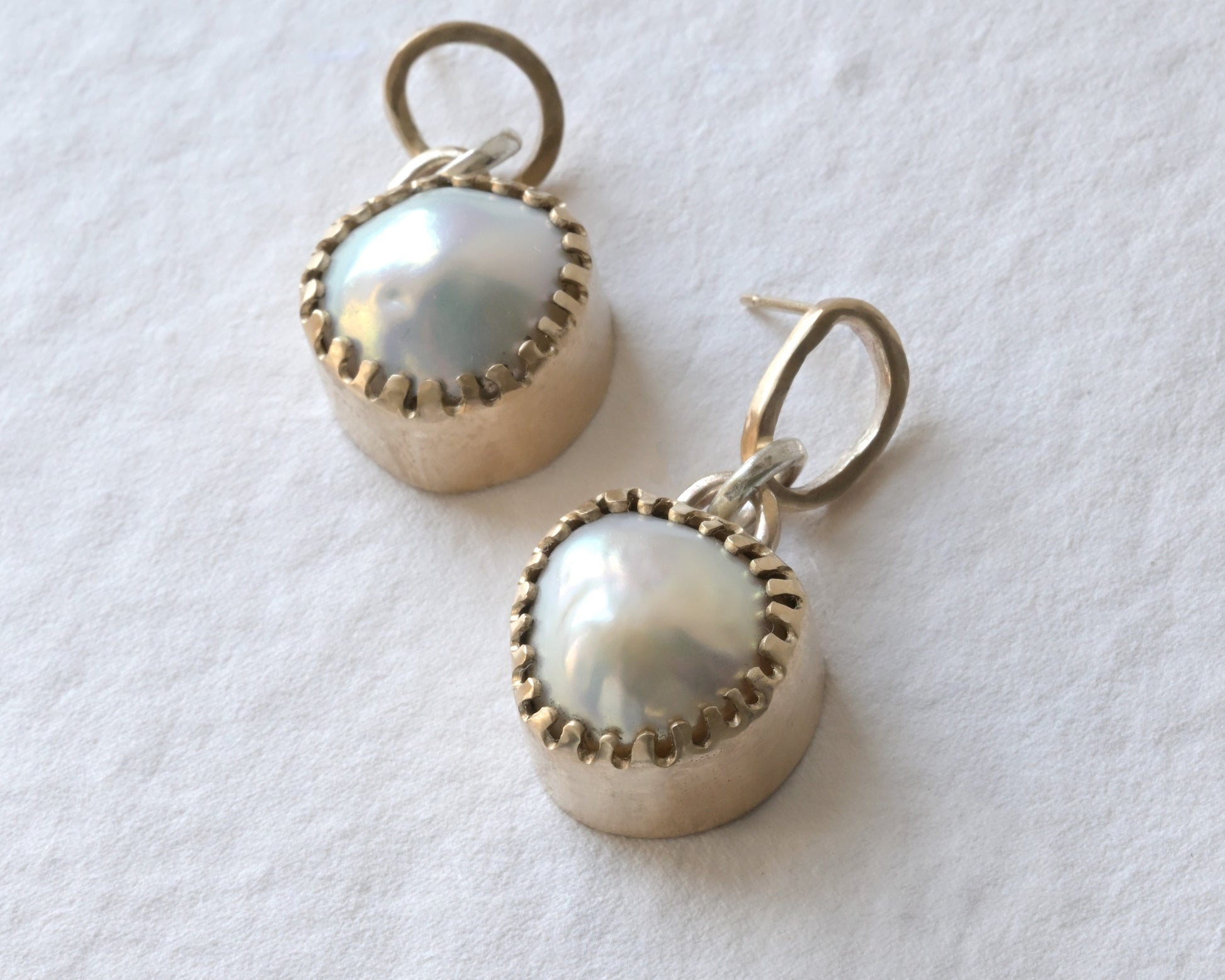 very big pearl earring encased in yellow gold placed on white cotswold white stone.