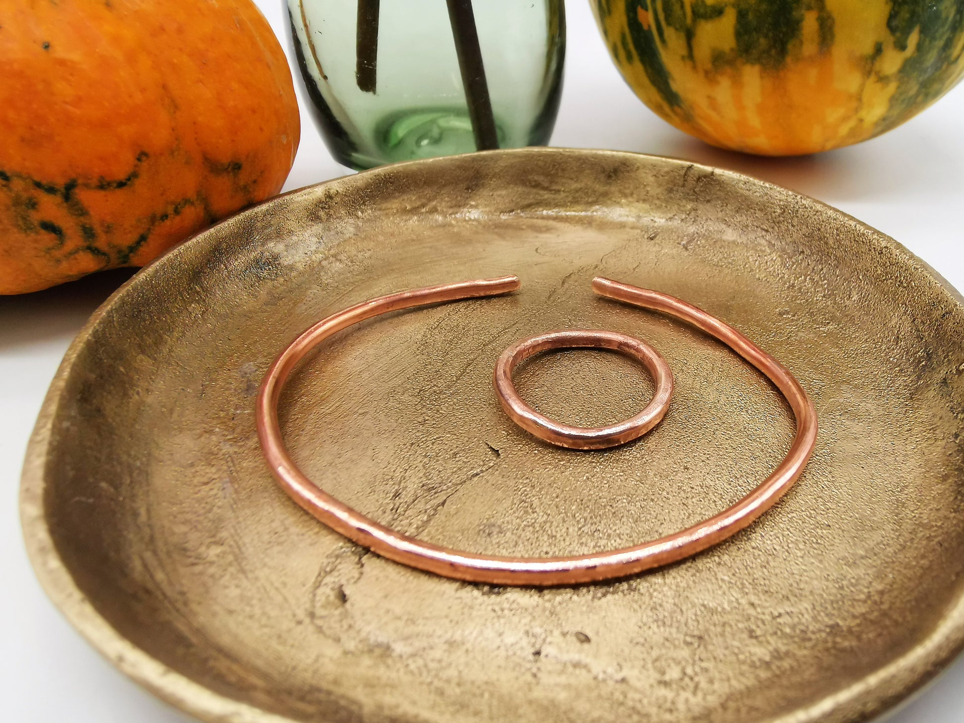 Handmade copper cuff and copper ring photographed together on a gold tray with pumpkins in the background.