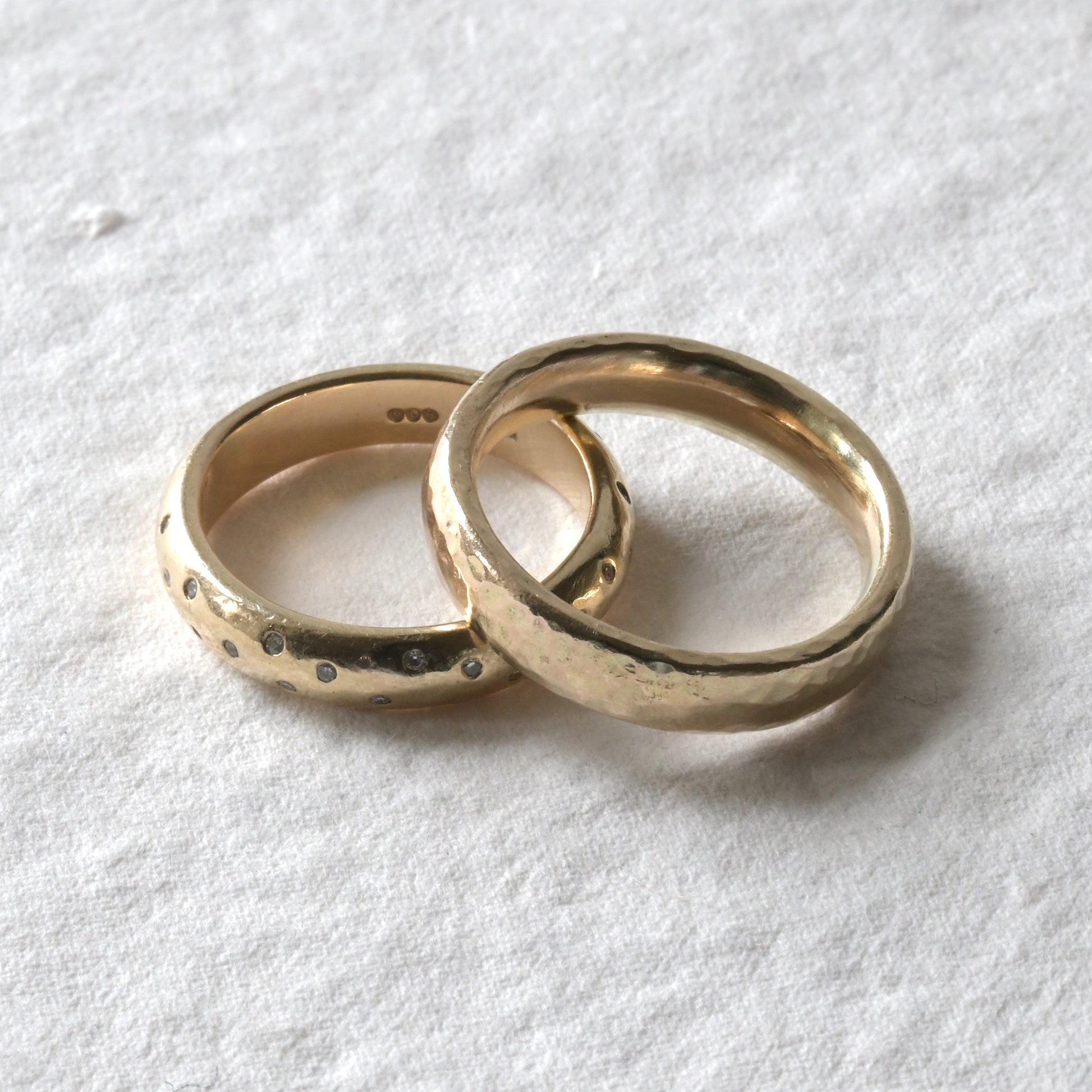 two yellow gold wedding rings stacked against each other pictured on white, ne with diamonds and one without.