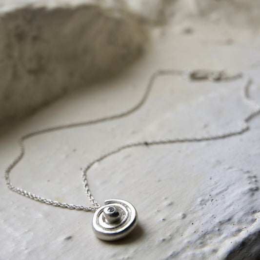 sterling silver diamond spiral pendant pictured on white brick in the Cotswold's. Handmade fine jewellery by Madeleine.