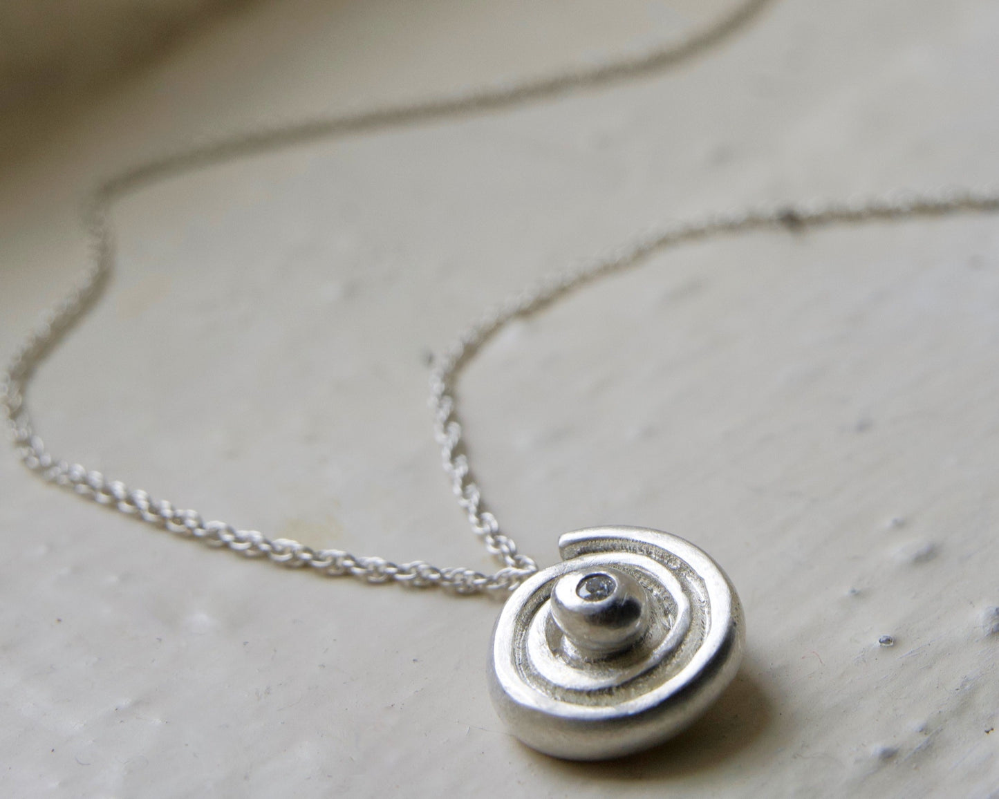 spiral silver diamond necklace photographed on white brick. Handmade fine jewellery by Madeleine.